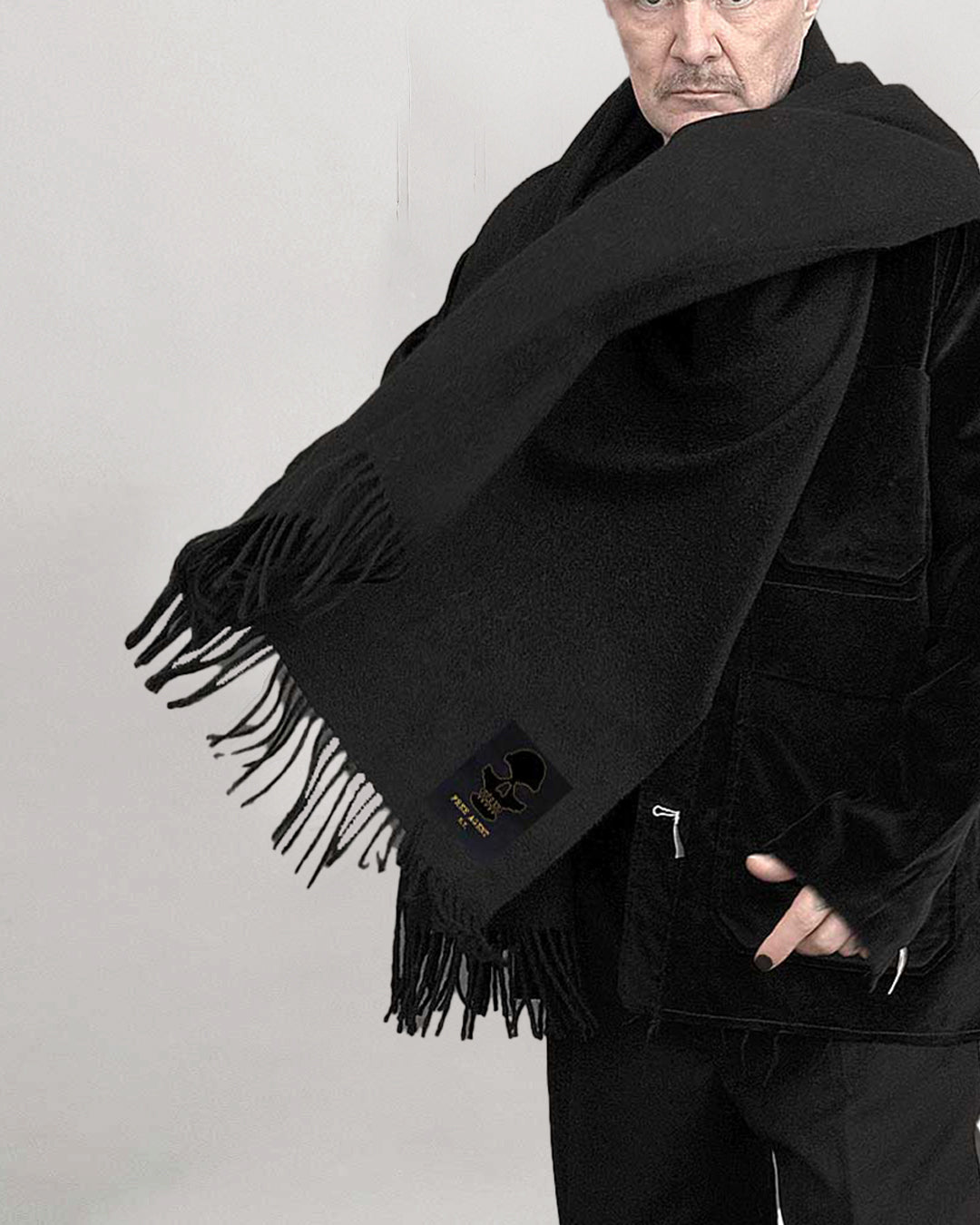 Person wearing a black scarf with fringes and a brand logo on a plain background